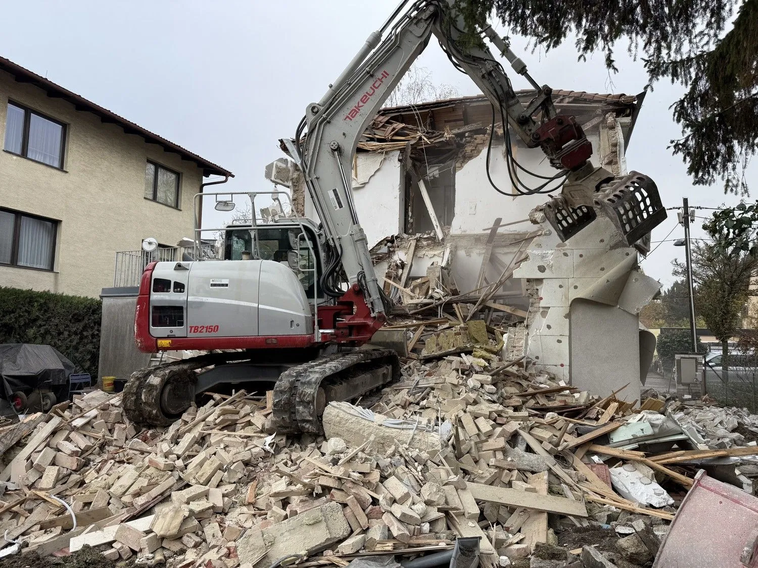 Bagger mit Abbruchzange vor einem halb abgetragenen Haus